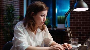 Weary accountant struggling to remain awake at workspace desk while inputting data on laptop, panning shot. Close up of exhausted businesswoman yawning in office while working overnight, camera A photo