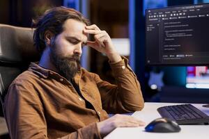 Tired man hurting from too much stress accumulated while doing software quality assurance, reading source code on computer. Developer suffers from headache after inspecting coding on PC for too long photo