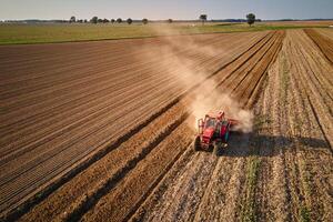 Red tractor working in agricultural field, cultivating and plowing dry soil, aerial view. Agribusiness concept. Small farming concept photo