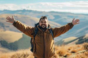 Male hiker reaching the summit of a hill with arms open wide, facing the horizon photo