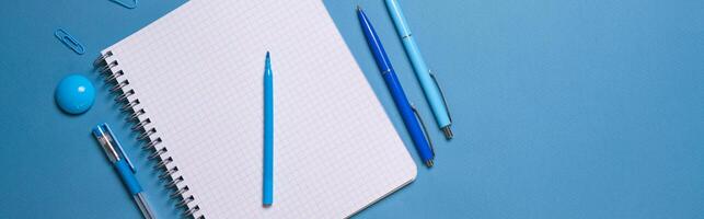Notebook and pen on a blue background. Top view with copy space. Stationery photo