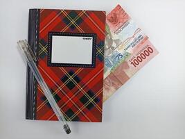 Wonosobo, Central Java Indonesia - August 9, 2024 Top view of pen, notebook and banknotes on white background. Indonesian Rupiah currency photo