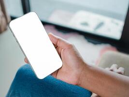Close-up image of a woman in jeans relaxed sitting in the cafe and using her smartphone. Smartphone white screen mockup for display your graphic banner, Mockup image blank white screen cell phone. photo