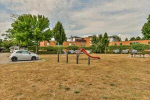 A grassy area with a playground and cars parked in front of it photo