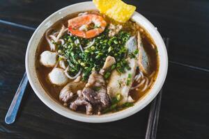 Tom Yum soup - Thai soup with prawns and rice noodles on wooden table in Vietnam photo