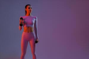Attractive fitness woman doing exercises with dumbbells on studio background and looking at side photo