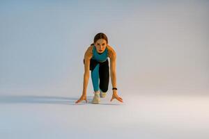 Female athlete in starting position ready for running looking at camera on studio background photo