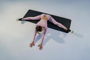 Flexible woman doing stretching exercises on yoga mat on studio background. Healthy lifestyle photo