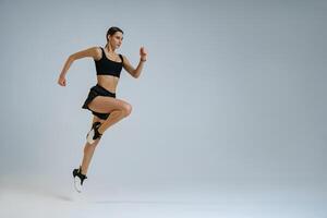 Determined sporty woman running in Mid-Air exercising during cardio workout over studio background photo
