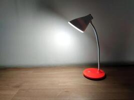 A modern red desk lamp with a white curved neck, powered by rechargeable batteries, emits soft LED light onto a wooden surface, creating a minimalist, cozy atmosphere. photo