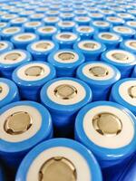 Close-up of blue cylindrical lithium batteries, featuring positive terminal tops, arranged in a precise, repeating grid. photo