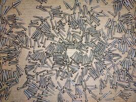 A high-resolution image of a pile of identical screws, showcasing their consistent size and shape. The screws are arranged in a unsorted pattern on a brown background. photo