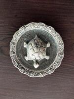 A top-angle view of a silver-plated tortoise figurine resting on a wooden surface, showcasing its intricate design and reflective finish against the rich wood grain. photo