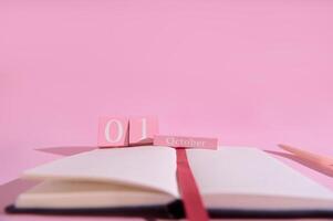 Pink themed calendar displaying the first of October with an open notebook and pencil in a minimalistic setting photo