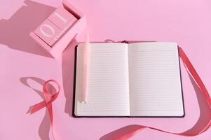 Open notebook with pen and ribbon on pink background showcasing October 1st theme photo