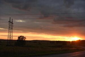 The evening landscape and the setting sun. High-voltage wires and an asphalt road in the evening. photo