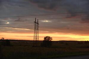 The evening landscape and the setting sun. High-voltage wires and an asphalt road in the evening. photo