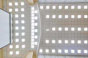 cassette stretched or suspended ceiling with square halogen spots lamps and drywall construction in empty room in house or office. Looking up view photo