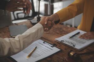Lawyer shaking hands with a client making about documents, contracts, agreements, cooperation agreements with a female client at the lawyer's desk and a hammer at the table. photo