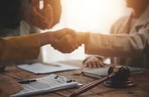 Lawyer shaking hands with a client making about documents, contracts, agreements, cooperation agreements with a female client at the lawyer's desk and a hammer at the table. photo
