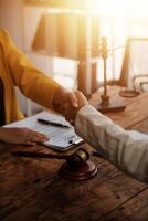 Lawyer shaking hands with a client making about documents, contracts, agreements, cooperation agreements with a female client at the lawyer's desk and a hammer at the table. photo