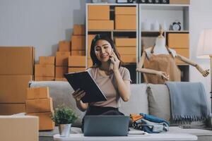 Asian SME business women use laptop computer checking customer order online shipping boxes at home. Starting Small business entrepreneur SME freelance. Online business, Work at home concept. photo