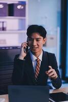 Serious trader using mobile phone app on smartphone for checking stock trading data analysis concept, focused businessman holding cellphone working in office with financial graph on computer monitors photo
