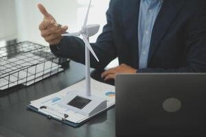 Shut of handsome business man working on new alternative energy development looking at a model of a wind turbine in modern startup. photo