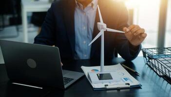 Shut of handsome business man working on new alternative energy development looking at a model of a wind turbine in modern startup. photo