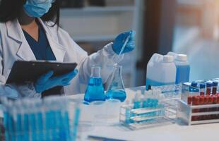 Group of dedicated scientist conduct chemical experiment in medical laboratory, carefully drop precise amount of liquid from pipette into test tube for vaccine drug or antibiotic development. Neoteric photo