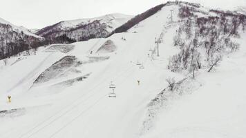 Aerial view of the ski resort with snowy mountain slopes and winter trees. A group of people going skiing and snowboarding down the hill at Didveli video