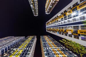 Low-angle view of colorful, illuminated high-rise buildings surrounding a dark night sky, showcasing modern architecture and urban living. photo