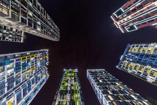 ángulo bajo ver de vistoso, iluminado Alto edificios rodeando un oscuro noche cielo, exhibiendo moderno arquitectura y urbano viviendo. foto