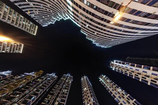 ángulo bajo ver de vistoso, iluminado Alto edificios rodeando un oscuro noche cielo, exhibiendo moderno arquitectura y urbano viviendo. foto