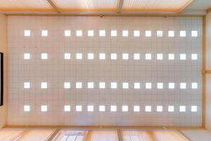 cassette stretched or suspended ceiling with square halogen spots lamps and drywall construction in empty room in house or office. Looking up view photo