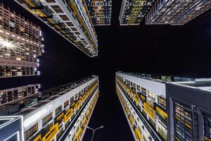 Low-angle view of colorful, illuminated high-rise buildings surrounding a dark night sky, showcasing modern architecture and urban living. photo