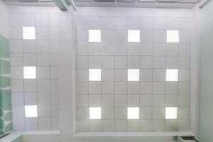 cassette stretched or suspended ceiling with square halogen spots lamps and drywall construction in empty room in house or office. Looking up view photo