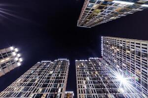 Low-angle view of colorful, illuminated high-rise buildings surrounding a dark night sky, showcasing modern architecture and urban living. photo