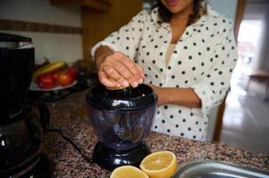 Woman preparing fresh lemon juice at home with an electric juicer in a modern kitchen setting with fruit in background photo