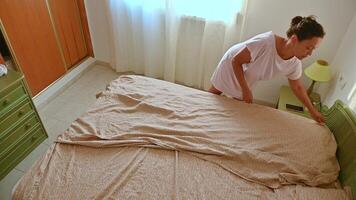 Woman making bed in a bright bedroom, showcasing daily routine and cleanliness in a cozy space with natural light streaming through the window. photo