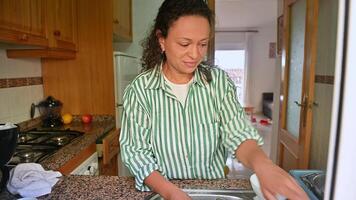 Woman in striped shirt performing daily tasks in a cozy kitchen setting, embodying routine and simplicity while showcasing a clean and organized lifestyle photo