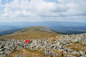 Mountainous terrain with large stones on the trail, marking the distance of the tourist route in the mountains, a flag for landmarks, a mountain system of ridges. photo