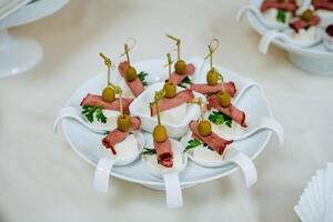 Appetizer on a plate, table setting for an event, ham and cheese on a skewer, pitted olive, catering for departure, beautiful serving of the dish. photo