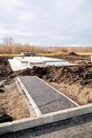 Stages of construction of a country house, construction site, asphalt path to the future house, concrete base cushion for a new country house. photo