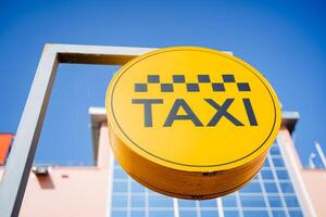 A taxi sign hangs on a pole, a yellow circle with the inscription taxi, the emblem of the checkers in black, the place where the car stops, the text of the taxi. photo