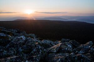 Morning dawn on the top of a stone mountain, the sun breaks through the first rays through the clouds, the dark silhouettes of the mountains in the distance, the glare of the sun. photo