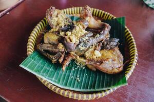 Traditional fried chicken with a yellow crispy condiment served on top of banana leaf. photo