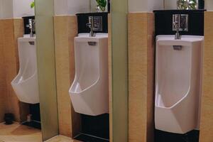 Three white urinals are lined up in a row in a public restroom with a partition between them. photo