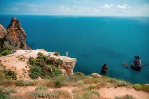 A woman stands on a cliff overlooking the ocean. The water is blue and the sky is clear. photo
