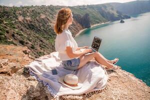 Freelance woman working on a laptop by the sea, typing away on the keyboard while enjoying the beautiful view, highlighting the idea of remote work. photo